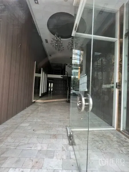 店屋 出租在Watthana, Bangkok - 玻璃门入口通向狭长商业空间，挑高天花与吊灯