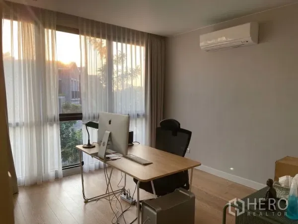联排别墅 出售在Lat Phrao, Bangkok - 采光充足的书房，书桌、落地窗、纱帘与木地板，壁挂空调。