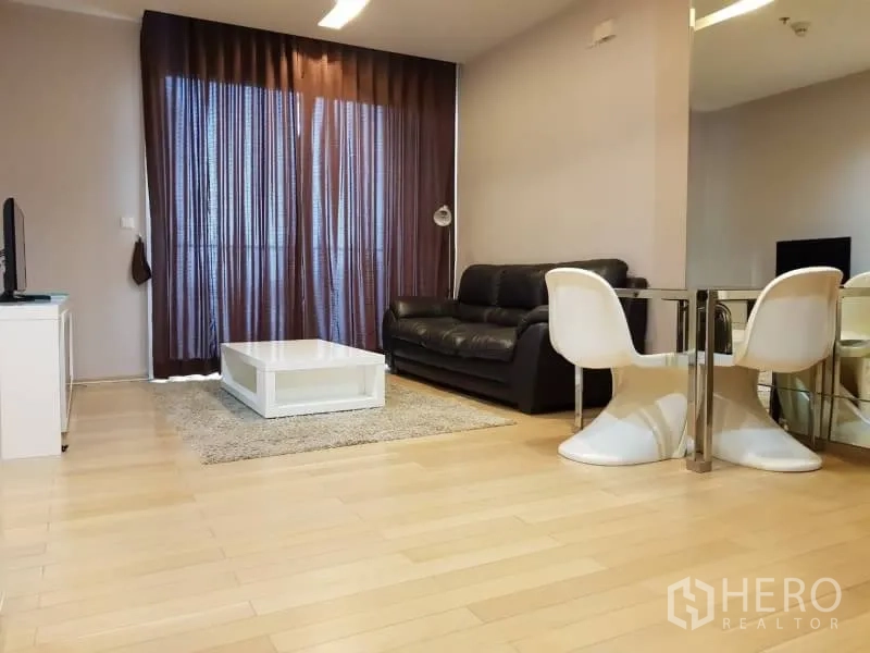 Condominium for rent in Khlong Toei, Bangkok - Open-plan living and dining area with leather sofa, round dining set, and floor-to-ceiling curtains.