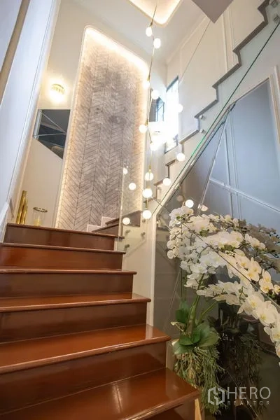 Detached House for sale in Pak Kret, Nonthaburi - Staircase with wooden steps, glass balustrade and modern orb pendant lighting.