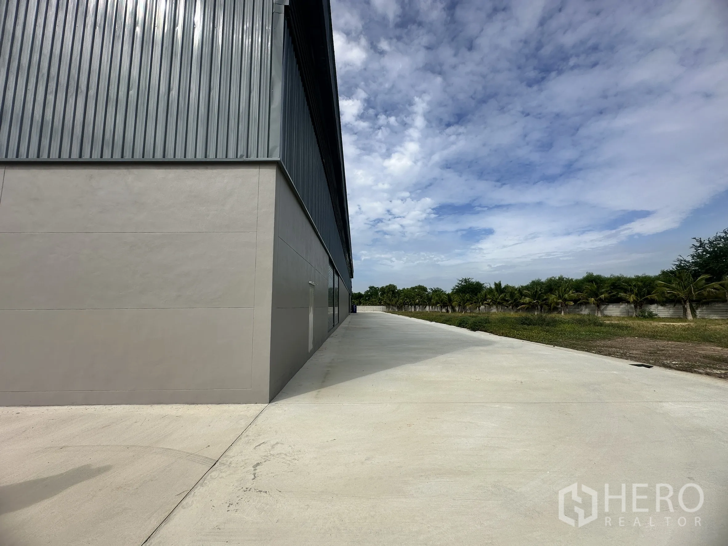 Factory for rent or sale in Bang Len, Nakhon Pathom - Long concrete driveway running beside the warehouse with trees along the boundary wall.