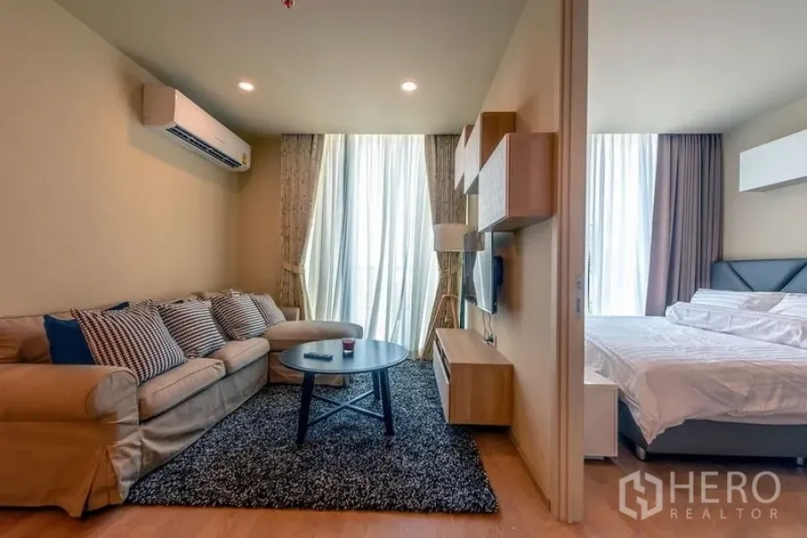 Condominium for rent in Watthana, Bangkok - Living room connected to bedroom via sliding door, bright curtains and comfortable sofa.